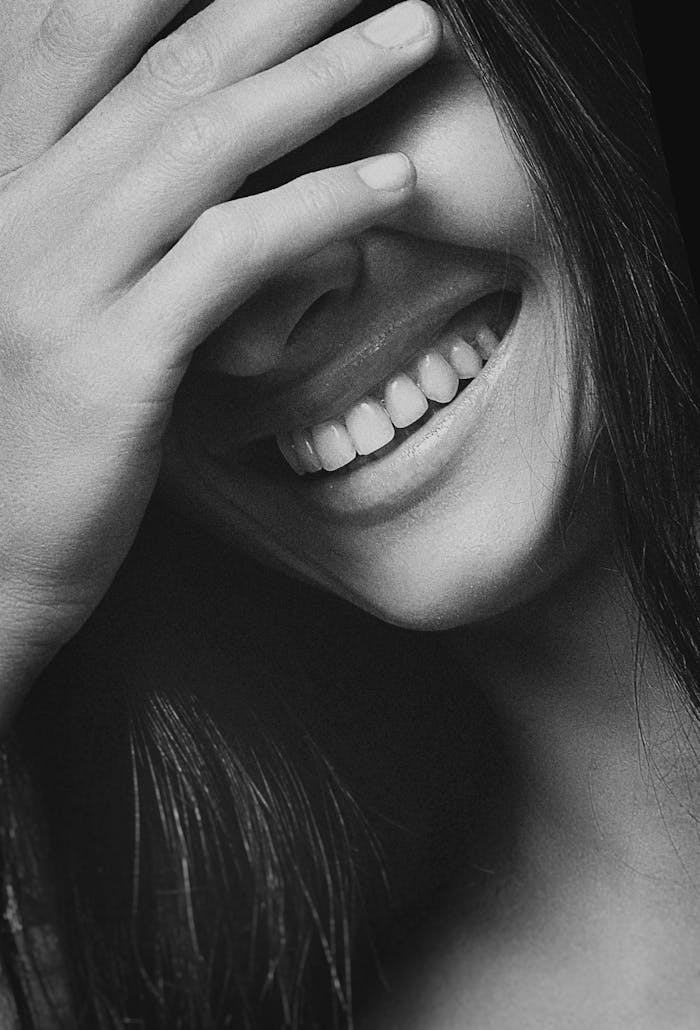 Artistic black and white close-up photo of a woman joyfully laughing with hand near face.
