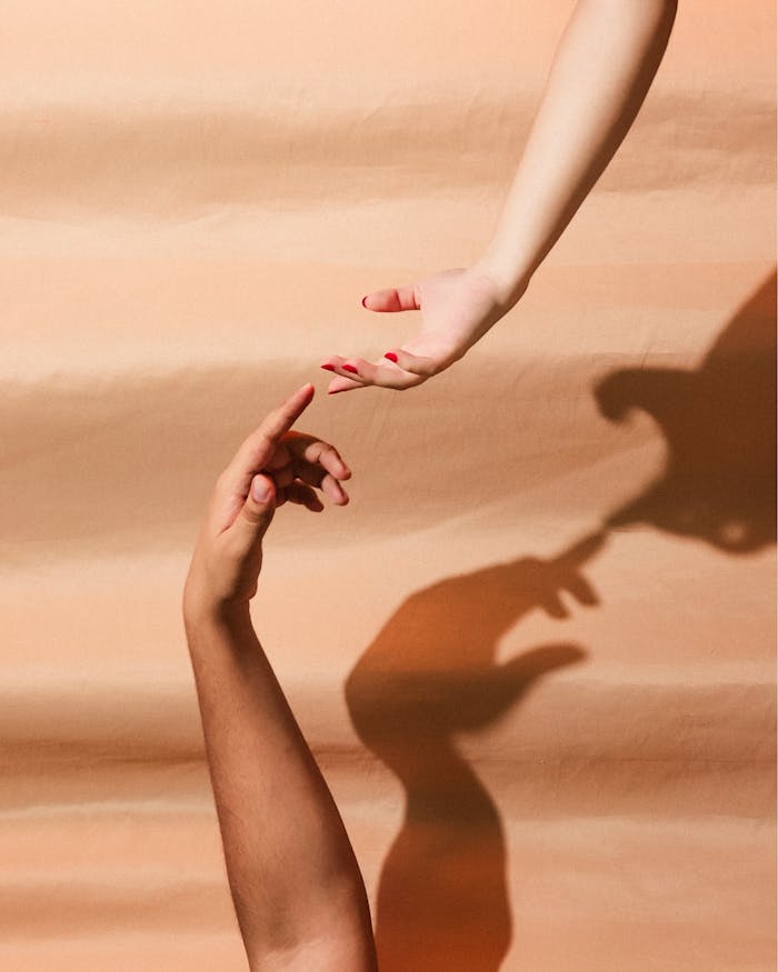 A conceptual minimalist image of two hands reaching towards each other with shadows on a peach background.